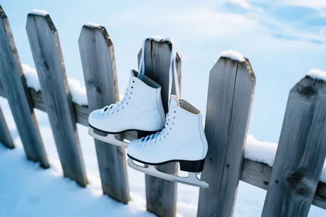 Een paar witte schaatsen hangt aan een verweerde houten omheiningspaal in een besneeuwd landschap met koele blauwe en witte tinten.