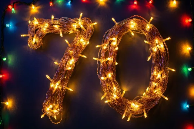 Het getal 70 is gemaakt van warme lichtjes tegen een donkere muur, met wazige gekleurde lichtjes op de achtergrond.