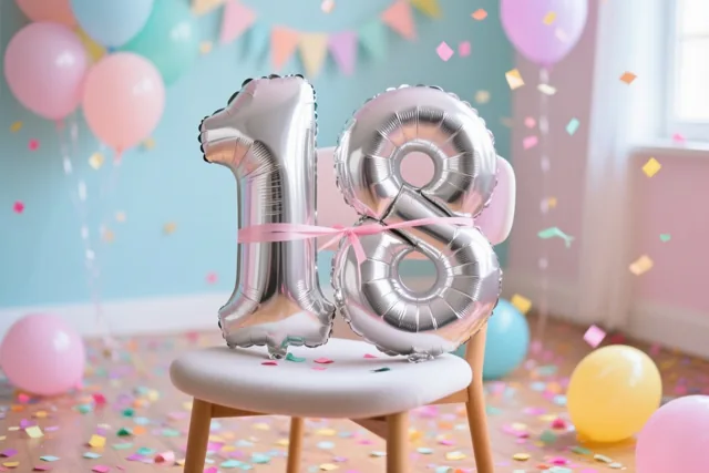 Zilveren cijferballonnen vormen 18 op een stoel met een roze lint, in een lichte kamer met kleurrijke confetti op de vloer en pastelballonnen errond.