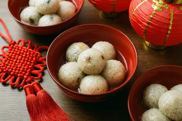 Rode kommen met zoete rijstballetjes staan op een houten tafel naast rode lantaarns en een rode Chinese sierknoop.