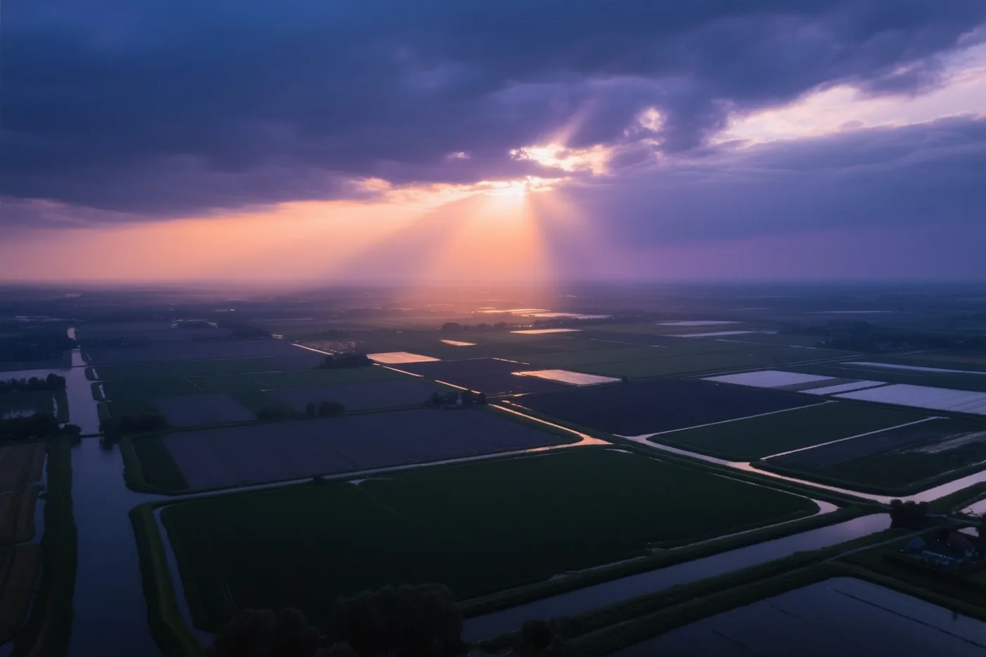 Een luchtbeeld toont geometrische velden en kanalen in een polderlandschap, waar zonlicht door donkere wolken breekt in paarse, oranje en groene tinten.