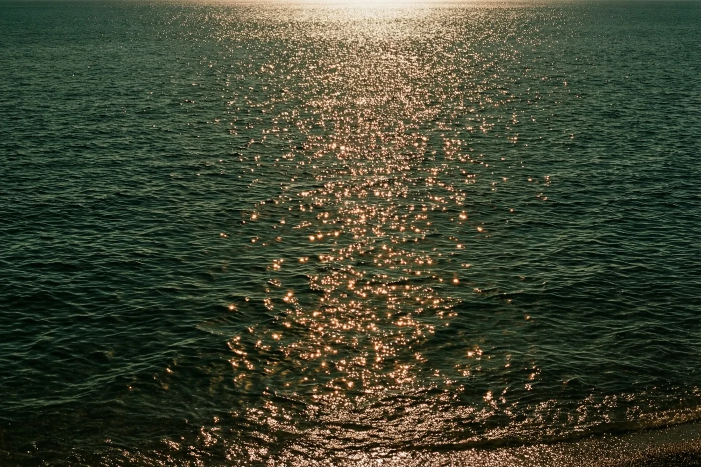 Zonlicht schittert in kleine lichtpunten op donkerblauw zeewater met zachte rimpelingen en een warme gouden gloed.