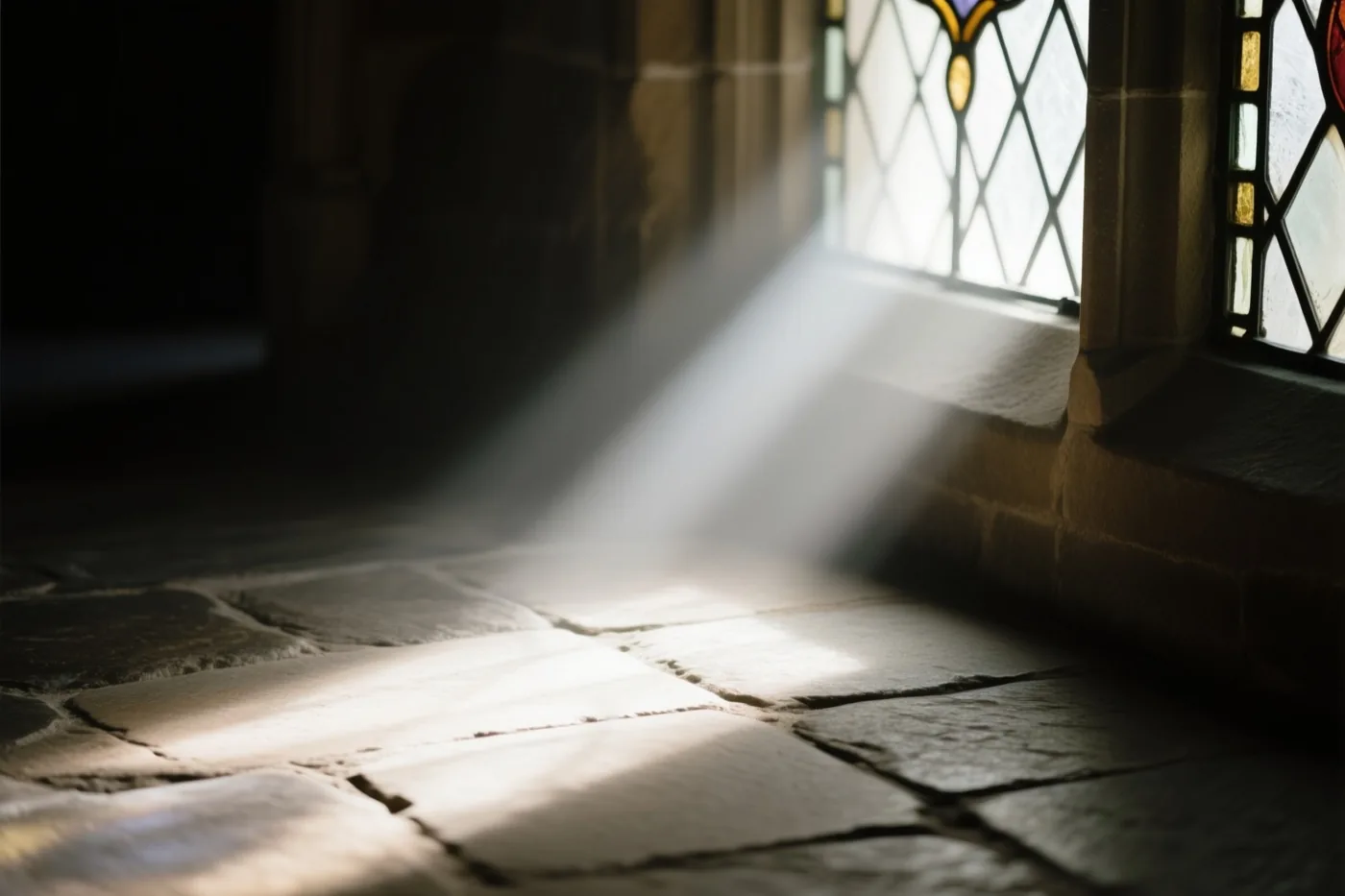 Een zonnestraal valt door een glasraam op een stenen vloer in een schemerig interieur met warme tinten en zachte schaduwen.