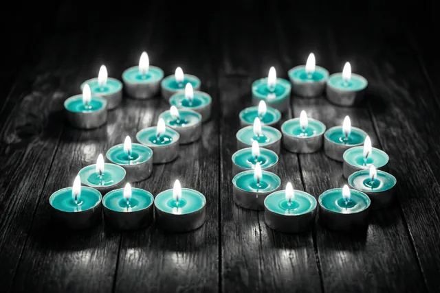 Brandende theelichtjes vormen 26 op een donkere houten vloer in een tafereel met blauwgroene en zwarte tinten.