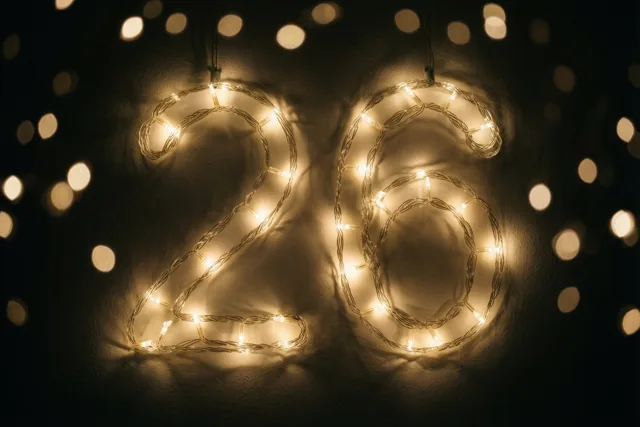 Warme lichtslingers vormen 26 tegen een donkere muur, met onscherpe feestlichtjes op de achtergrond.