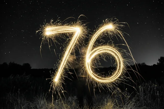 Gouden lichtsporen vormen 76 tegen een sterrenhemel, met donkere silhouetten van gras en bomen onderaan.