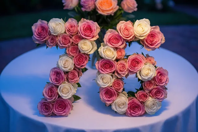 Roze en witte rozen vormen 76 op een wit tafelkleed in zachtblauw licht.