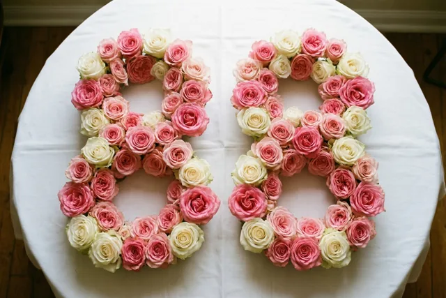 Twee grote achten van roze en roomwitte rozen liggen op een wit tafelkleed, recht van boven gefotografeerd.