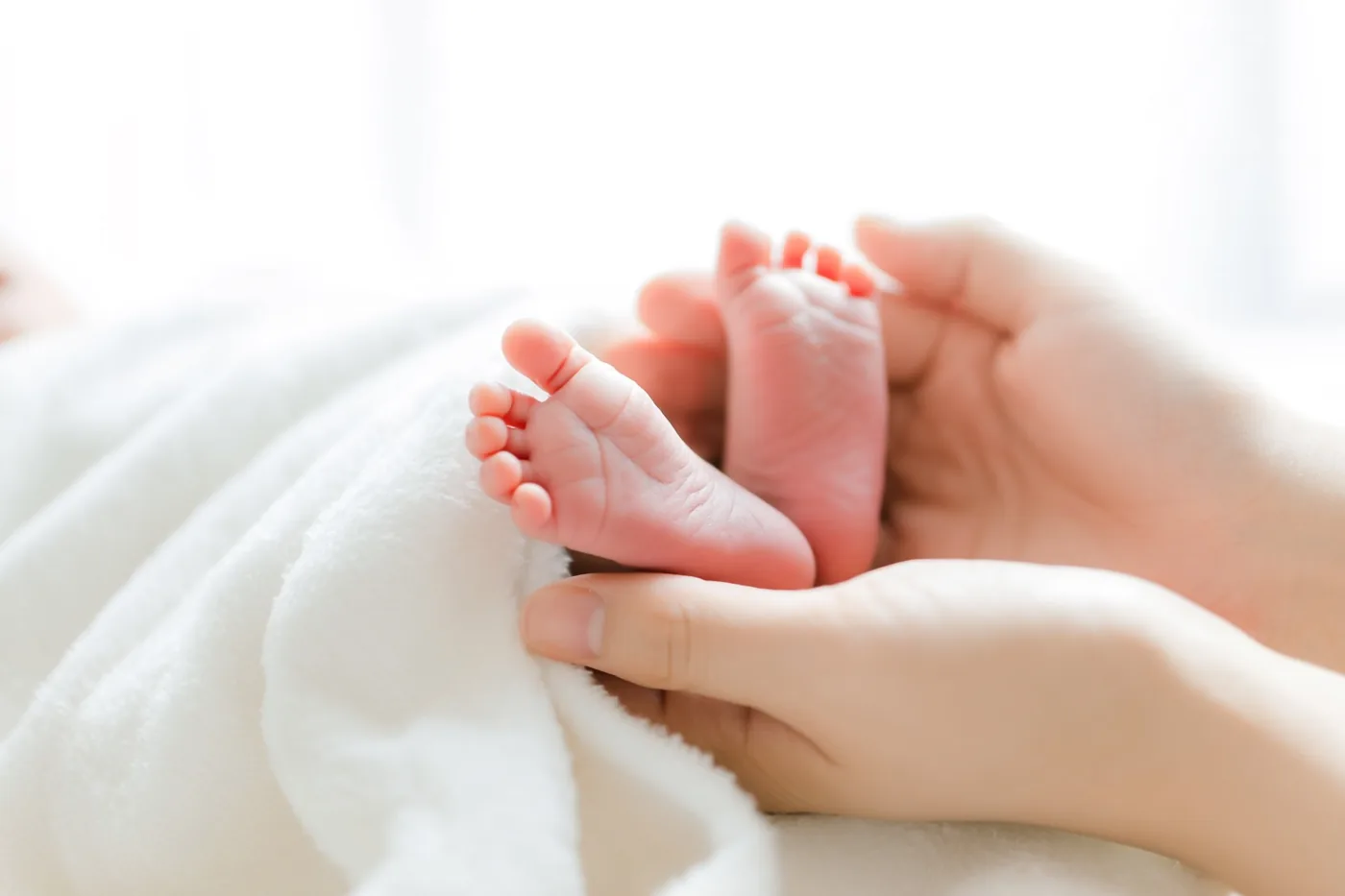 Twee kleine voetjes van een pasgeboren baby rusten in de handen van een volwassene op een zachte witte deken.