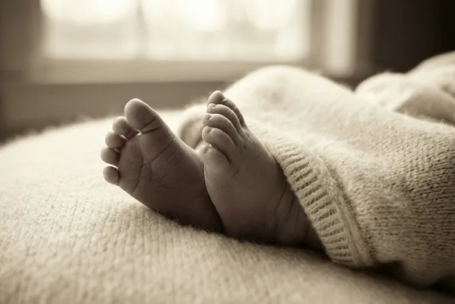 De kleine voetjes van een pasgeboren baby rusten op een lichte stof met structuur in zacht raamlicht.