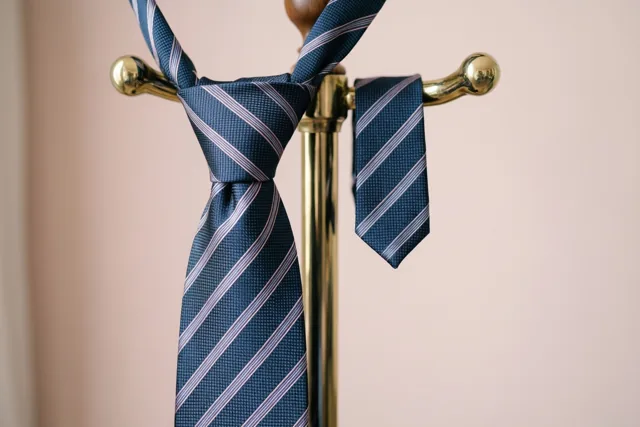 Een grote en een kleine bijpassende gestreepte das hangen aan een messing kledingstandaard tegen een zachtroze achtergrond.