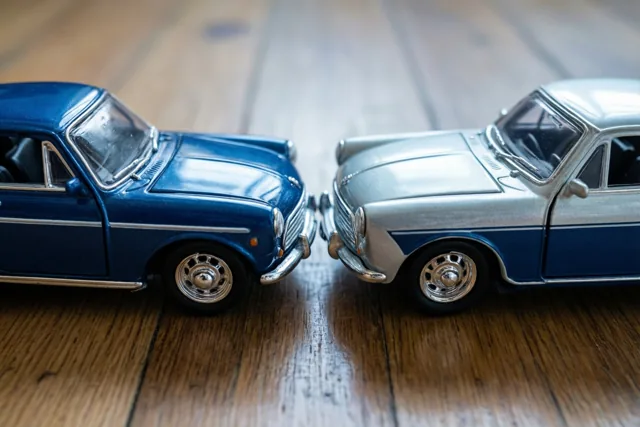 Twee blikken speelgoedauto's in retrostijl, in blauw en zilver met chroomdetails, staan met de neuzen naar elkaar op een houten vloer.