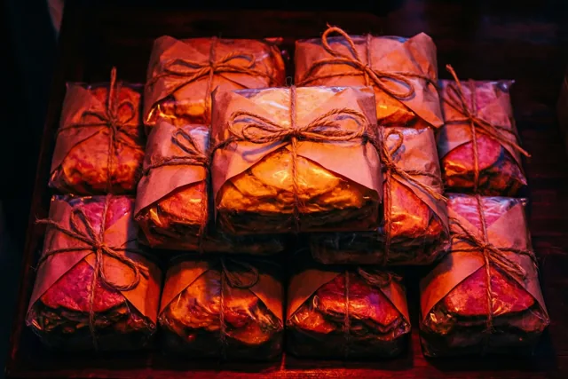 Een stapel voedselpakketjes in bruin papier met touw ligt op donker hout in warm roodachtig oranje licht.