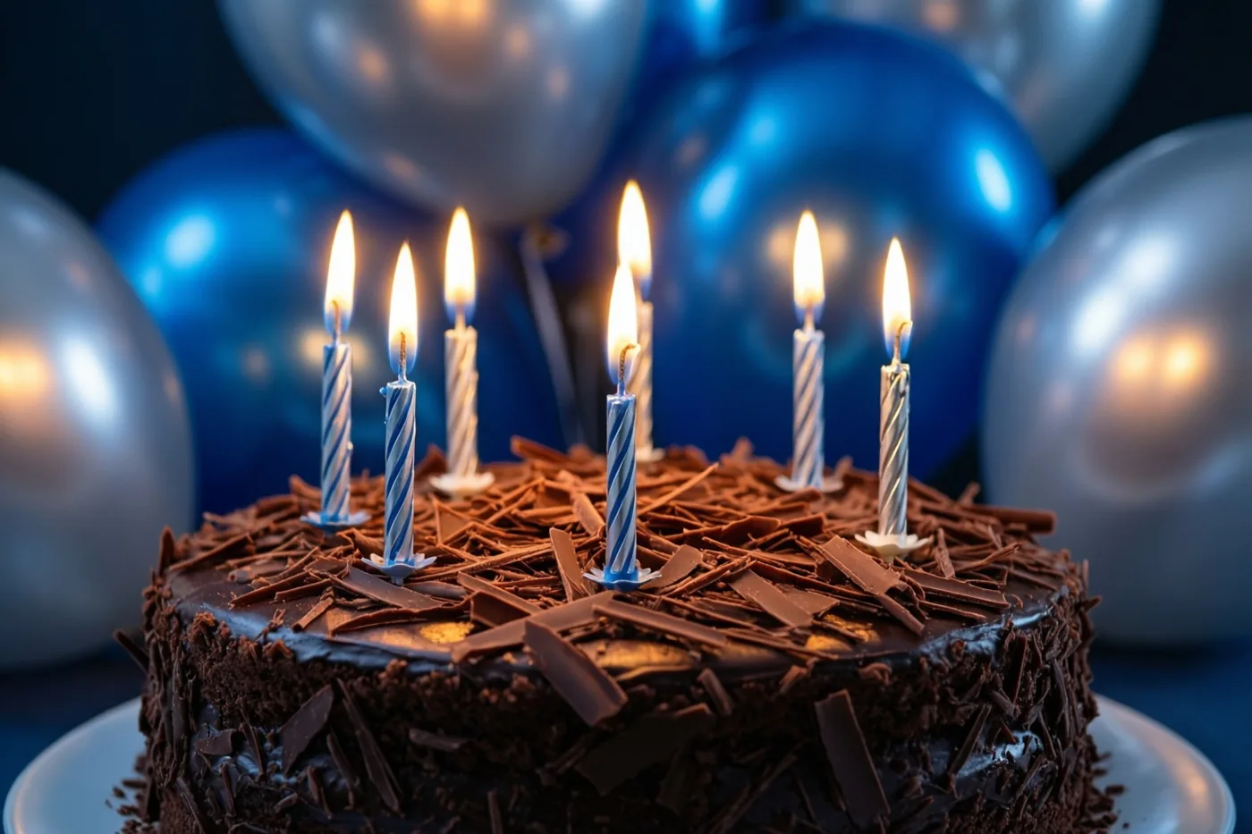 Een chocoladetaart met chocoladeschilfers en brandende blauw-wit gestreepte kaarsjes staat voor onscherpe blauwe en zilverkleurige ballonnen.