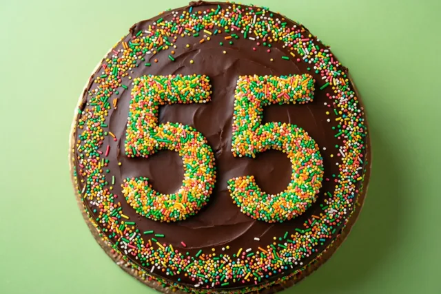 Van bovenaf is een ronde chocoladetaart met 55 van kleurrijke suikerstrooisels te zien tegen een effen lichtgroene achtergrond.