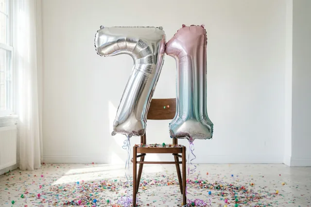 Twee grote folieballonnen in de vorm van 7 en 1 zijn vastgemaakt aan een houten stoel in een lichte kamer met confetti op de vloer.