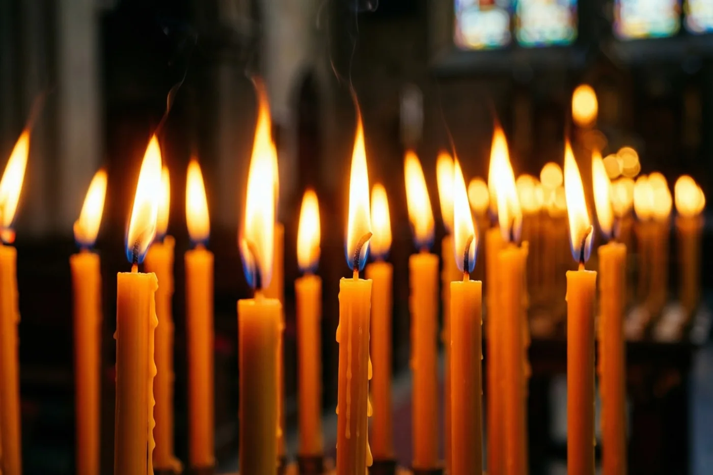 Een rij brandende communiekaarsen met onscherpe vlammen verspreidt oranje en geel licht in een donkere kerk.