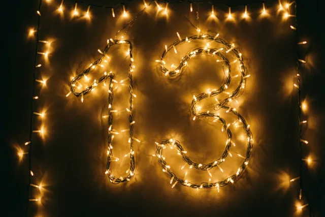 Goudgele lichtjes vormen 13 tegen een donkere muur, met zachte onscherpe lichtvlekken eromheen.
