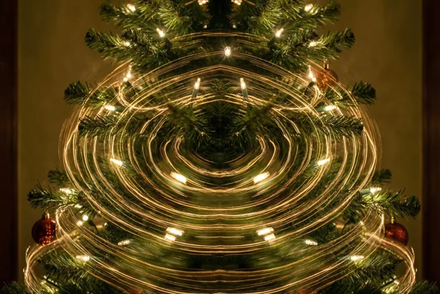 Rond een langzaam draaiende kerstboom met groene naalden en rode versiering vormen de lichtjes gouden strepen in een warm verlichte binnenruimte.