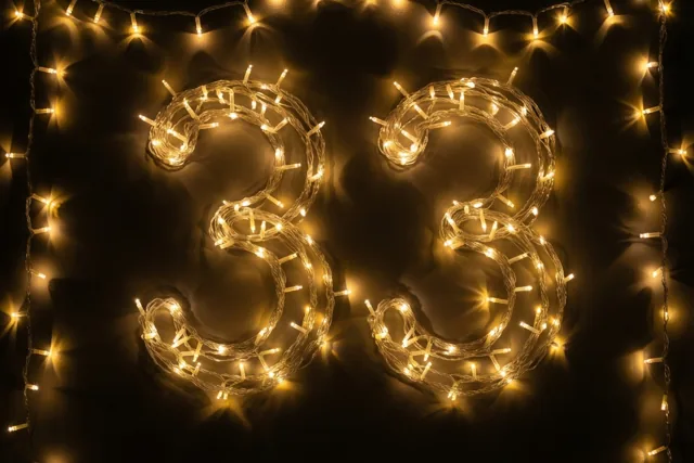 Warmgele lichtslingers vormen het getal 33 op een donkere muur, omkaderd door een rand van dezelfde lichtjes.