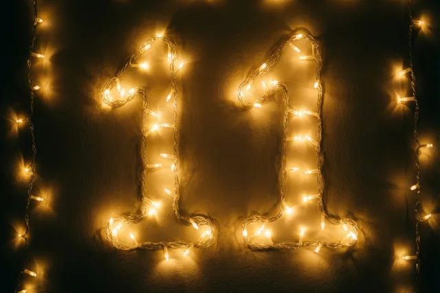Warme goudgele lichtjes vormen 11 tegen een donkere muur met structuur, met onscherpe lichtvlekjes eromheen.