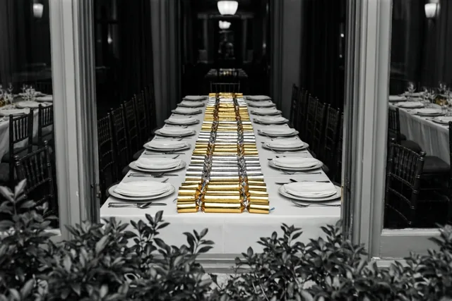 Door een deuropening is een lange tafel te zien met witte borden en gouden en zilveren feestcrackers in het midden, met groen op de voorgrond.