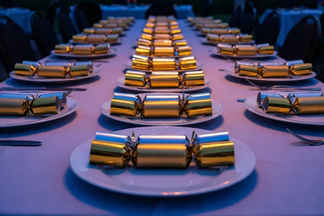Een lange tafel met witte borden en gouden en zilveren feestcrackers wordt verlicht door blauw sfeerlicht.