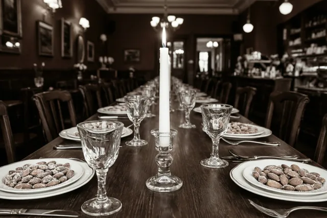 Een lange houten tafel in een bruin café is gedekt met witte borden met suikeramandelen, kristallen glazen en één brandende witte kaars in het midden.