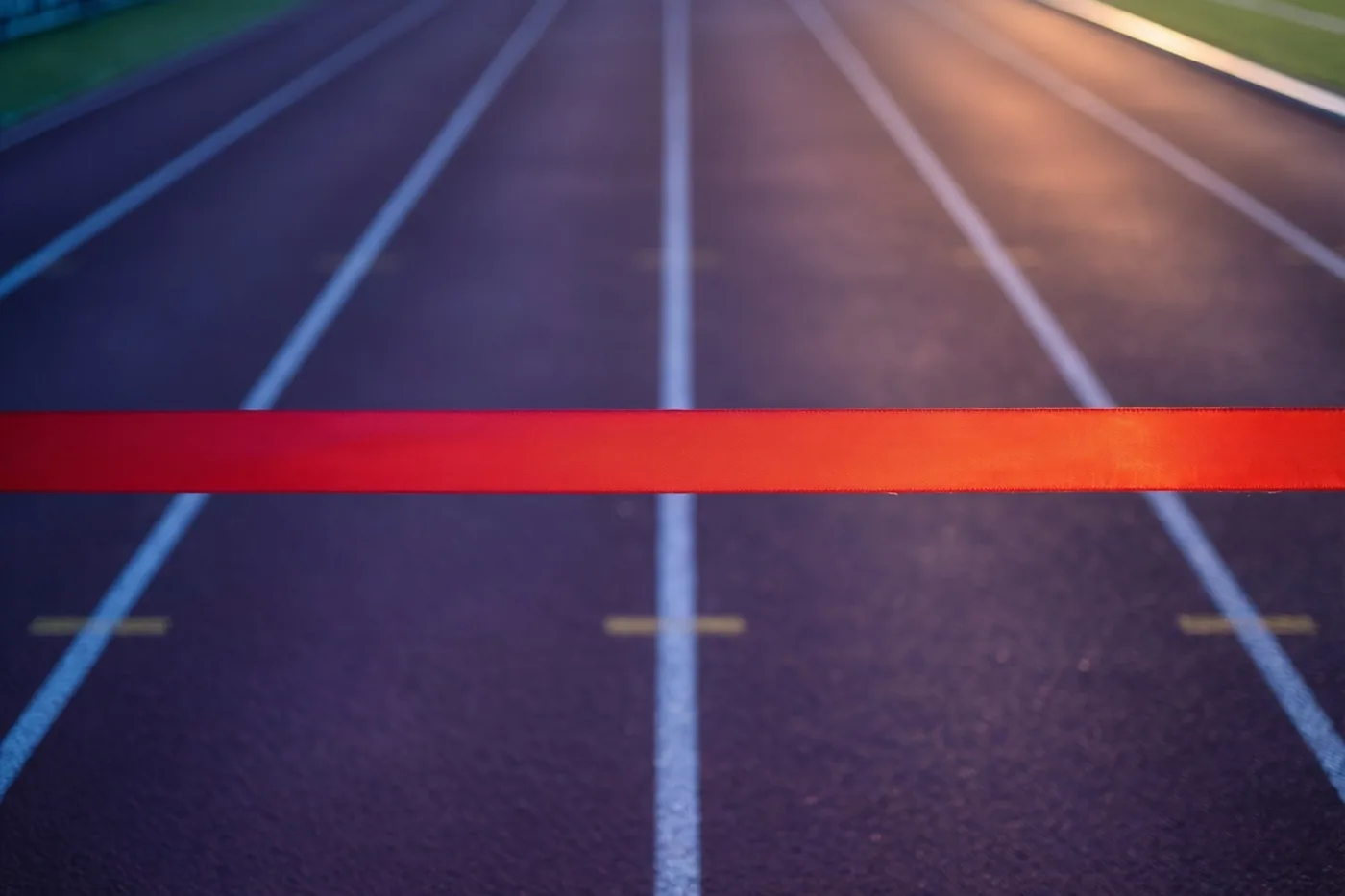 Een rood finishlint is over een donkerblauwe atletiekbaan met witte baanlijnen gespannen, gezien vanuit een laag standpunt.