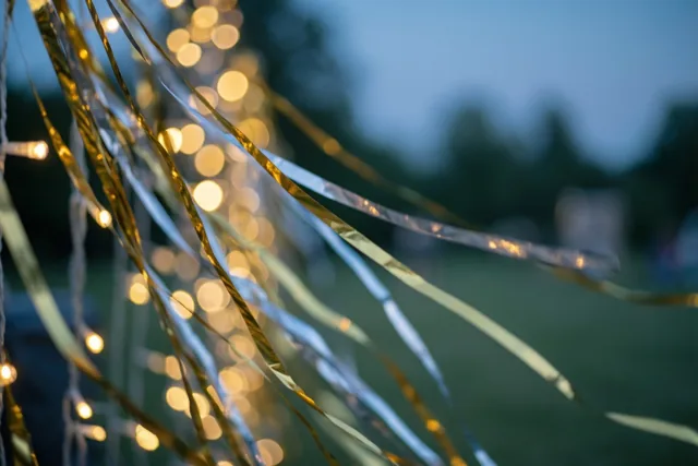 Gouden en zilveren metallic slingers staan voor wazige warme lichtjes en groen onder een koele blauwe schemerhemel.