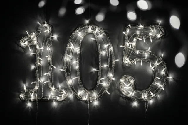 Lichtslingers vormen een gloeiende 105 tegen een donkere muur, met onscherpe lichtjes op de achtergrond.