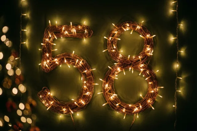 Het getal 58 is gemaakt van warm gloeiende lichtjes tegen een donkere muur met wazige lichtvlekken op de achtergrond.