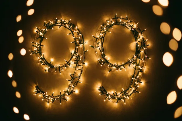 Het getal 99 is gevormd met warm gloeiende lichtslingers op een donkere muur, met onscherpe lichtpunten op de achtergrond.