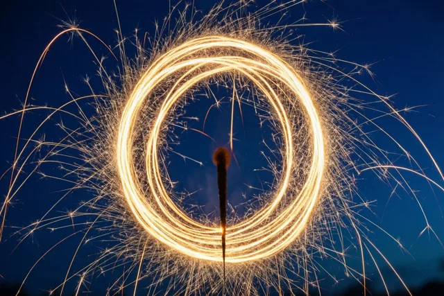 Goudkleurige lichtsporen van sterretjes draaien in cirkels tegen een diepblauwe nachthemel.