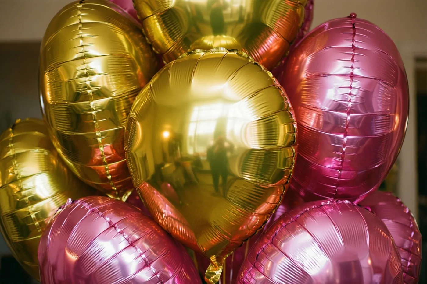 Glanzende gouden en roze folieballonnen zitten dicht bij elkaar en weerspiegelen elkaar in zacht feestlicht.