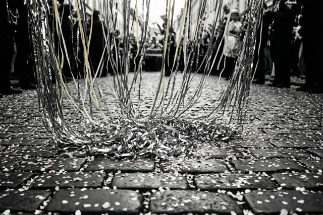 Zilveren en gouden serpentines hangen boven en liggen op kasseien met confetti, in een zwart-wit beeld met selectieve kleur.