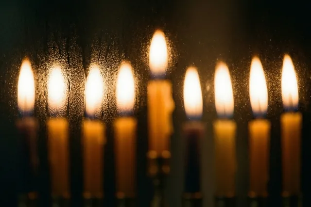 Een kandelaar met negen brandende kaarsen is door matglas te zien als zachte gouden en oranje lichtvlekken in het donker.