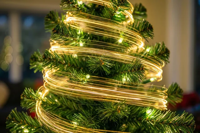 Een close-up toont groene naalden van een langzaam draaiende kerstboom met gouden lichtstrepen die rond de takken kringelen.