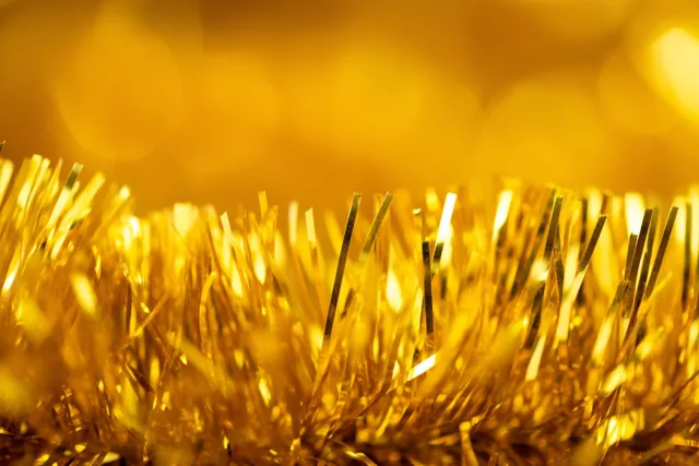 Sliertjes van een gouden glitterslinger weerkaatsen fel licht tegen een zacht vervaagde gouden achtergrond.