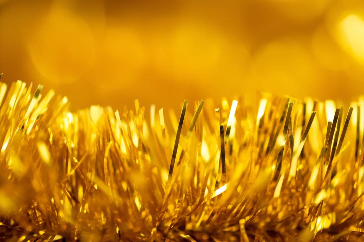 Sliertjes van een gouden glitterslinger weerkaatsen fel licht tegen een zacht vervaagde gouden achtergrond.
