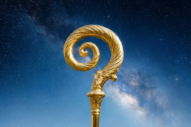 Een gouden bisschopsstaf met een grote spiraal staat tegen een diepblauwe sterrenhemel waarin de Melkweg zichtbaar is.