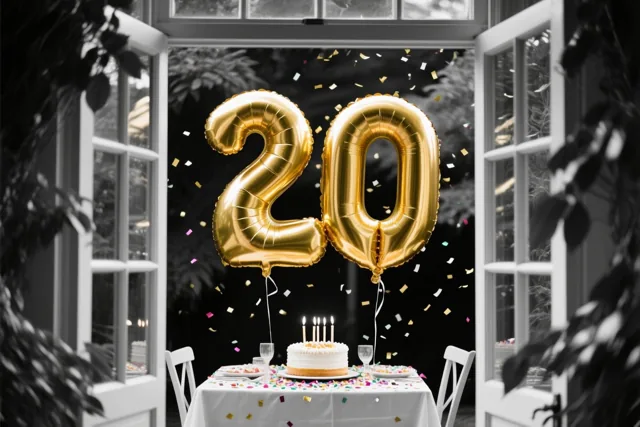 Door een open raam is binnen een feesttafel met taart en confetti te zien, met grote gouden folieballonnen in de vorm van 20 tegen een zwart-witte achtergrond.