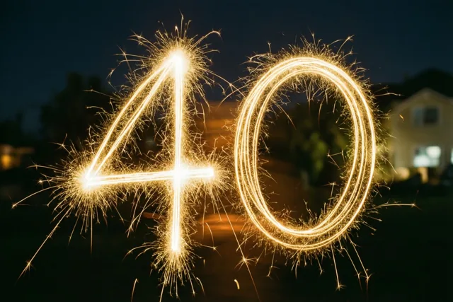 Gouden lichtsporen vormen 40 tegen een donkere nachthemel, met een onscherp huis op de achtergrond.