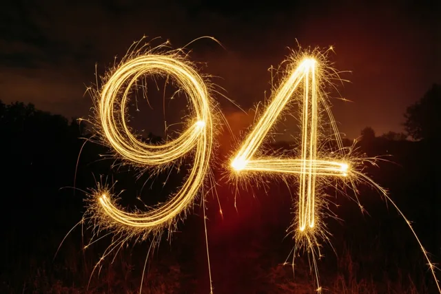 Gouden lichtsporen van sterretjes vormen 94 tegen een donkere nachtlucht, met silhouetten van bomen op de achtergrond.