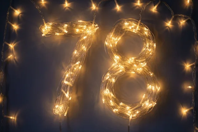Warme lichtslingers vormen 78 tegen een donkere muur, met zachte onscherpe lichtvlekken in goudgele tinten.