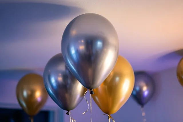 Goudkleurige en zilverkleurige metallic ballonnen zweven bij zacht licht tegen een wit plafond.