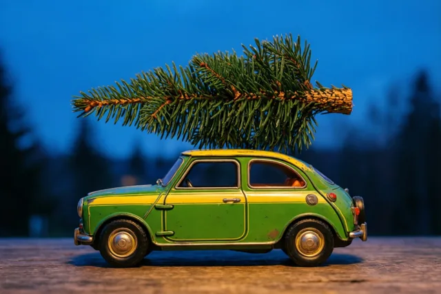 Een groen-geel blikken speelgoedautootje in vintagestijl met een dennentak op het dak staat in warm licht tegen een blauwe schemerachtergrond.