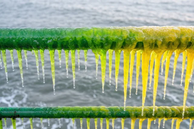 IJspegels met een kleurverloop van groen naar geel hangen aan een leuning boven een grijze zee.
