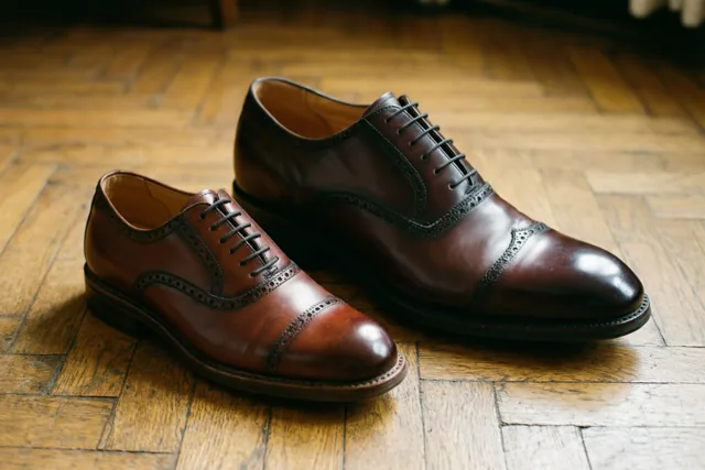 Een groot paar gepoetste donkerbruine brogues en een kleiner paar lichtbruine brogues staan naast elkaar op een houten parketvloer.
