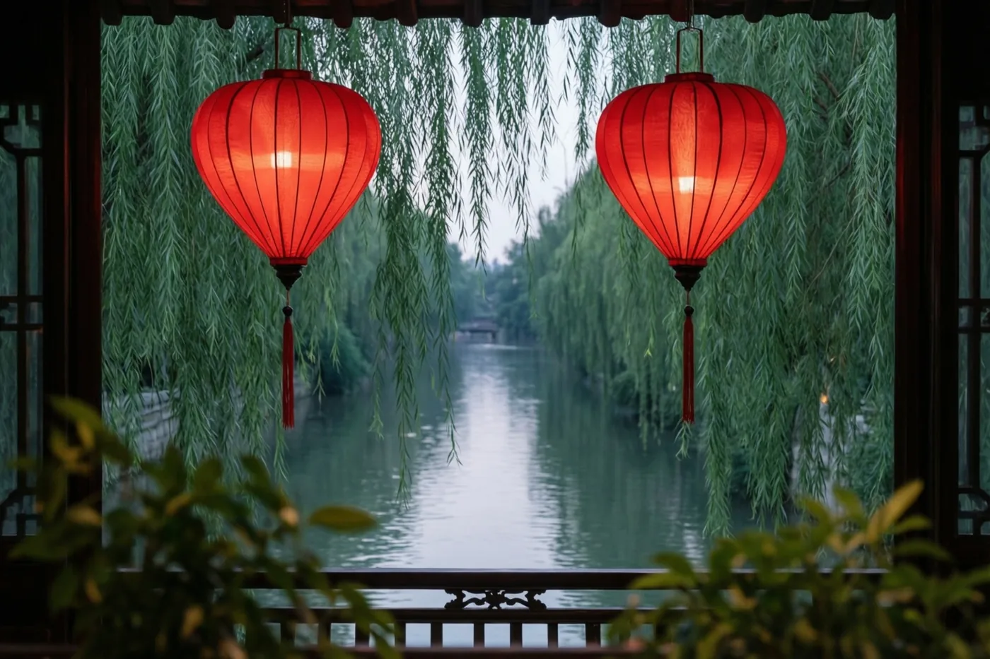 Twee verlichte rode hartvormige lantaarns hangen onder een houten dakrand, tussen treurwilgentakken aan een rustige rivier in de schemering.